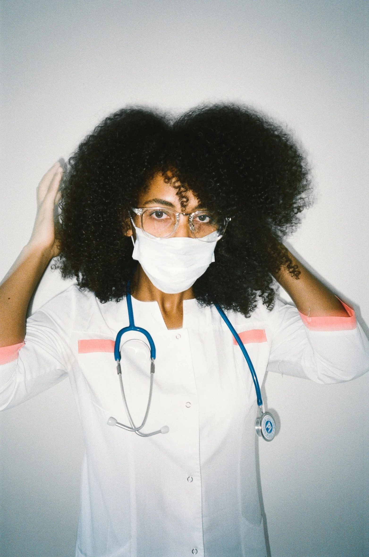 a woman with a stethoscope covering her face, an album cover, inspired by Dr. Atl, trending on pexels, mixed race, white uniform, frizzy hair, masked doctors