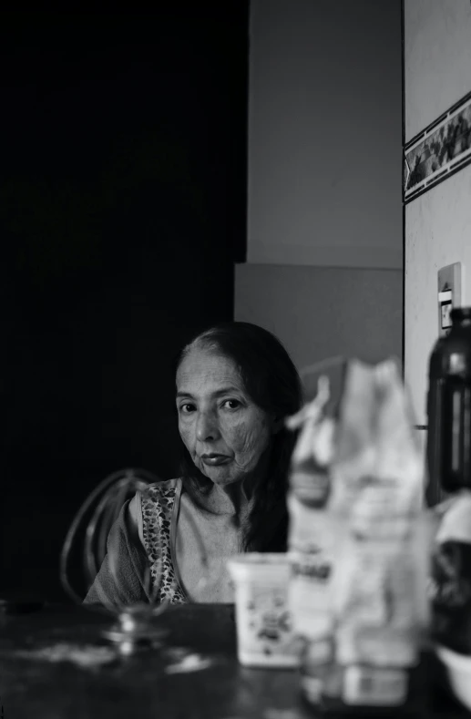 a black and white photo of a woman sitting at a table, by Giorgio Cavallon, dayanita singh, gongbi, looking content, performance