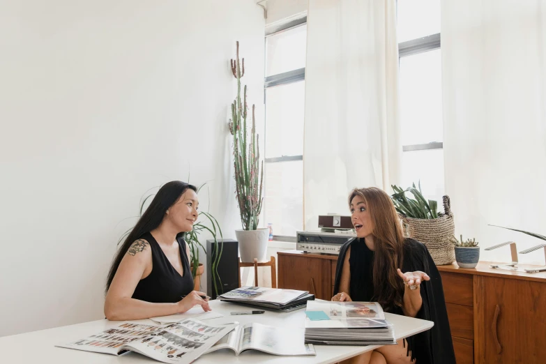 two women sitting at a table talking to each other, pexels contest winner, in a white room, 9 9 designs, location in a apartment, sydney hanson