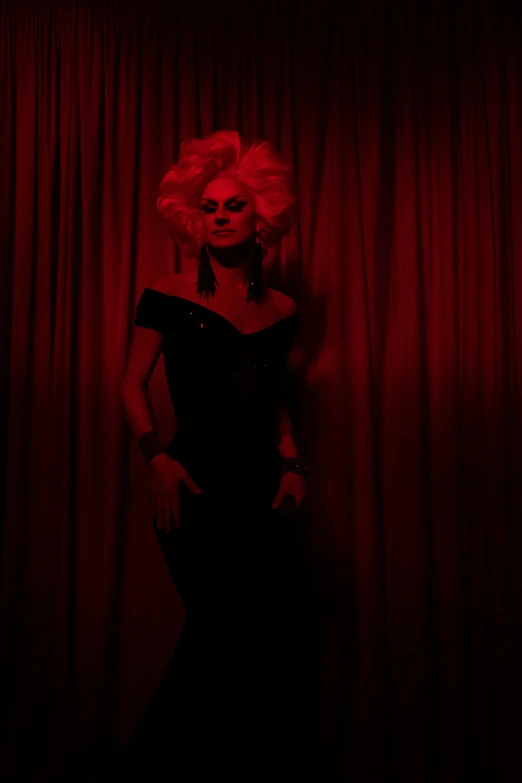 a woman standing in front of a red curtain, an album cover, inspired by Nan Goldin, pexels, transgressive art, ru paul\'s drag race, dark dress, evil look, square