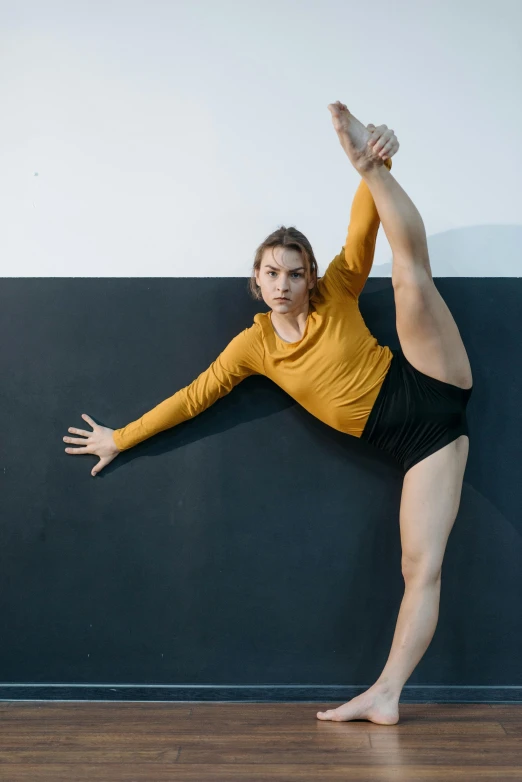 a woman in a yellow shirt is doing a yoga pose, inspired by Elizabeth Polunin, lachlan bailey, square, on a black wall, sydney sweeney