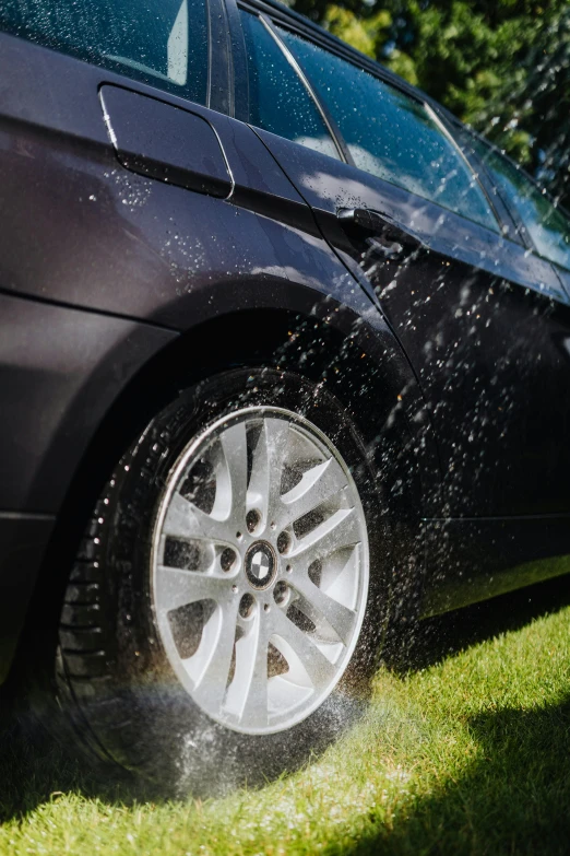 a car is sprinkled with water from a hose, pexels contest winner, detailed alloy wheels, black car, brown, side view close up of a gaunt