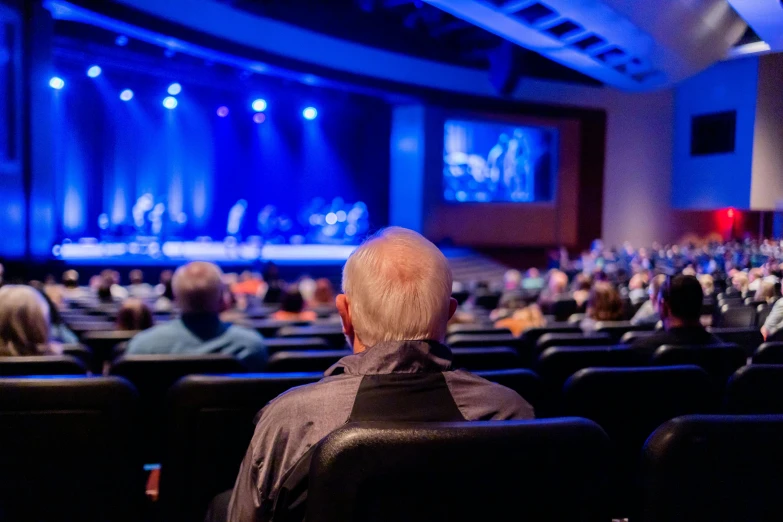 a group of people sitting in front of a stage, pexels, scene from church, older male, man sitting facing away, photo of a beautiful