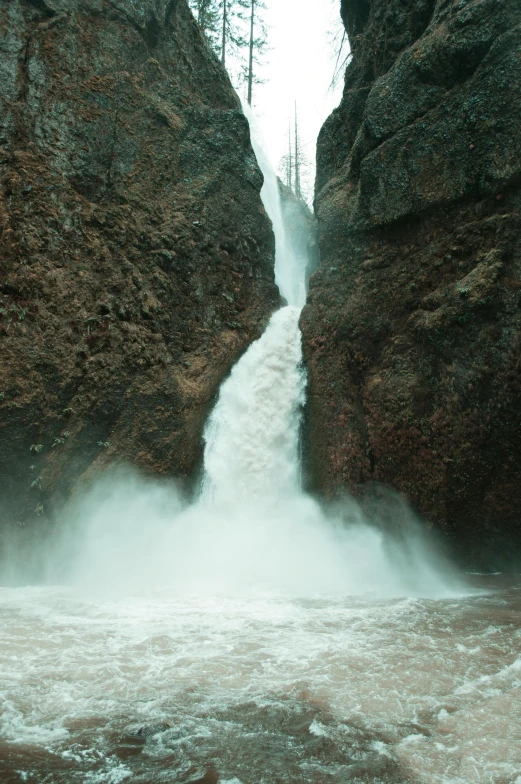 a man standing in front of a waterfall, brown water, wyoming, rushing water, in between a gorge