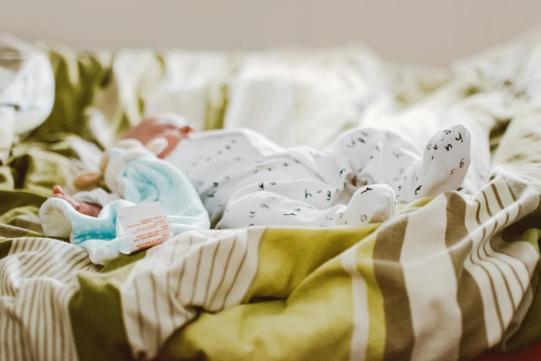 a pile of baby clothes sitting on top of a bed, by Ruth Simpson, unsplash, in hospital bed, tiny feet, profile image, conjoined twins