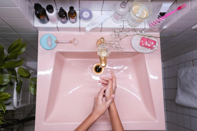 a person washing their hands in a pink sink, by Julia Pishtar, apothecary, silicone skin, golden glow, high - angle view