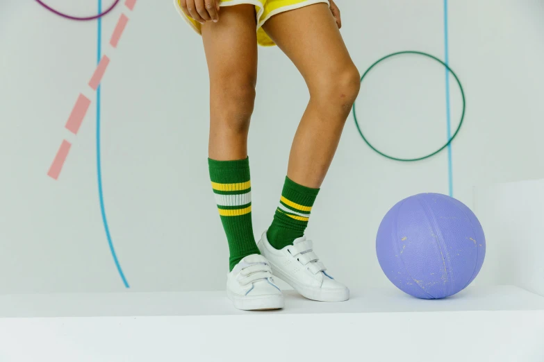 a woman standing next to a purple ball, dribble, striped socks, yellow and olive color scheme, bella poarch, wearing green clothing