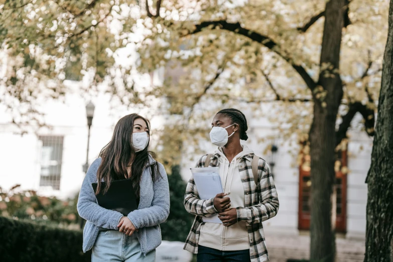 two people walking down a sidewalk wearing face masks, a photo, by Emma Andijewska, trending on pexels, happening, college girls, people looking at a house, diverse, a person standing in front of a