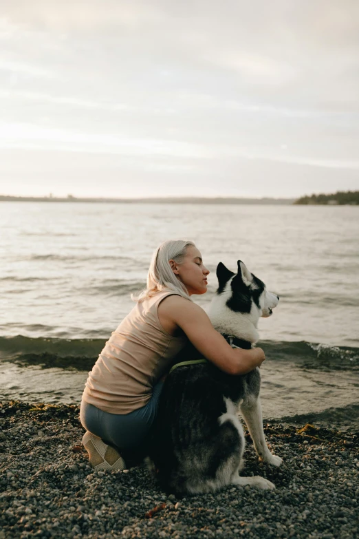 a woman sitting on the beach with her dog, pexels contest winner, siberian husky, tenderness, non-binary, scandinavian