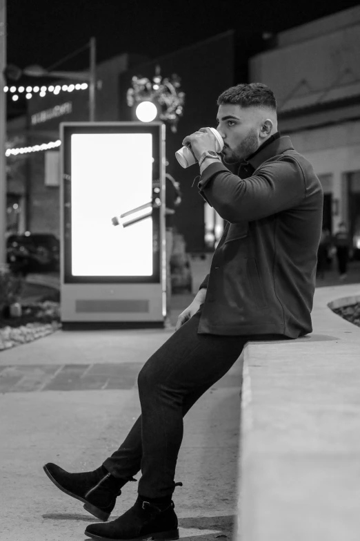 a man sitting on a ledge drinking from a cup, a black and white photo, by Andrew Stevovich, wearing a track suit, at a mall, thicc, attractive pose