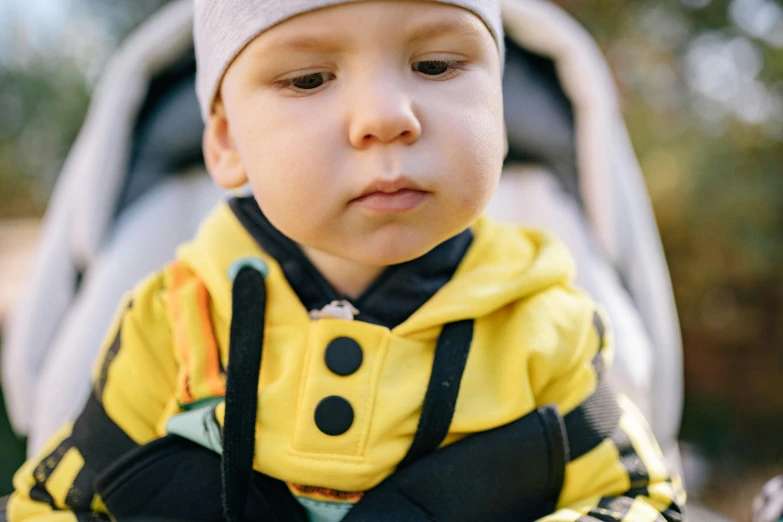 a close up of a child in a stroller, by Julia Pishtar, unsplash, yellow overall, handsome, thumbnail, serious focussed look