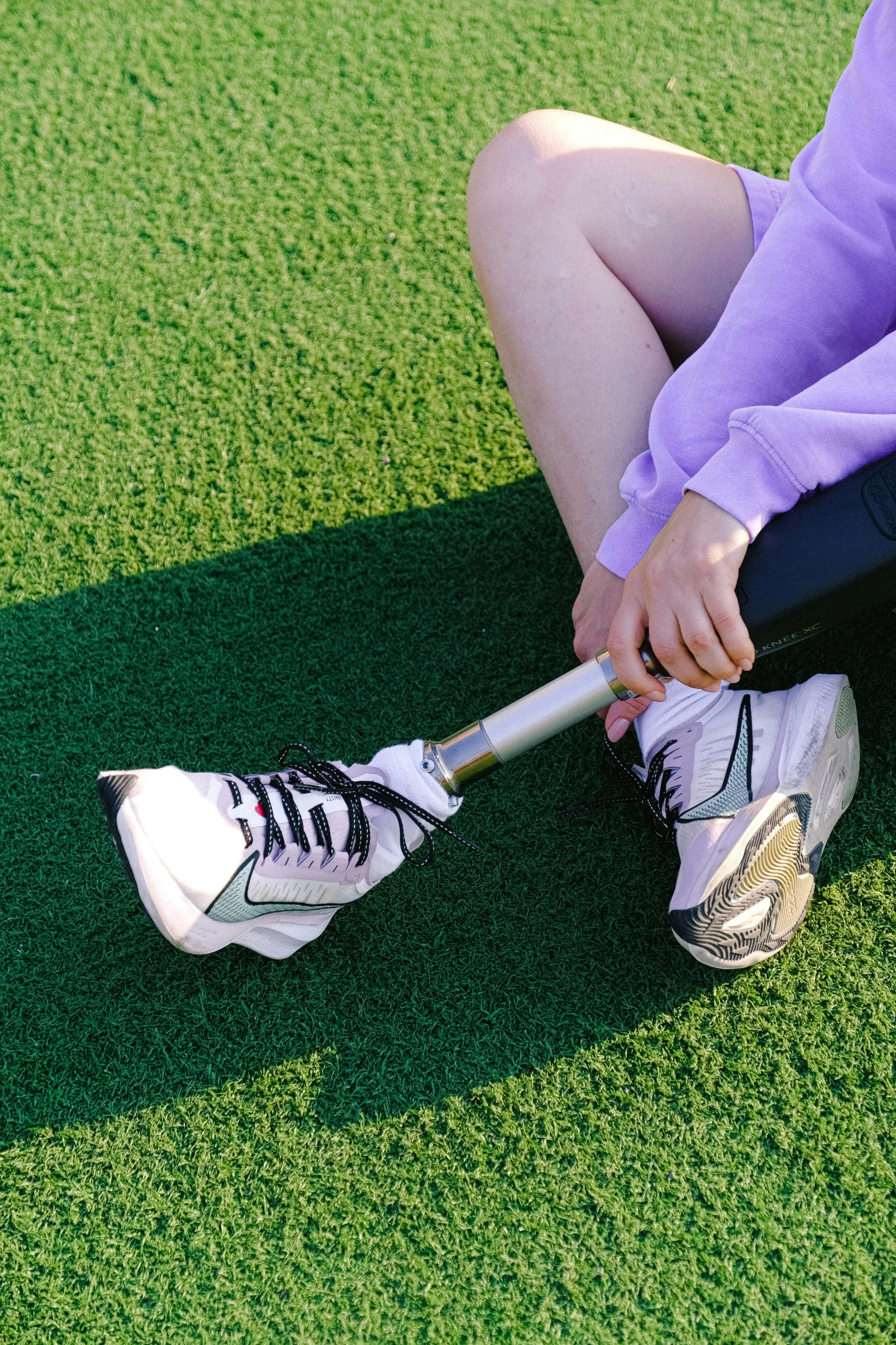 a woman sitting on the ground holding a baseball bat, inspired by Ren Hang, trending on pexels, futuristic sneakers, grass - like, robotic prosthetic limbs, y2k aesthetic