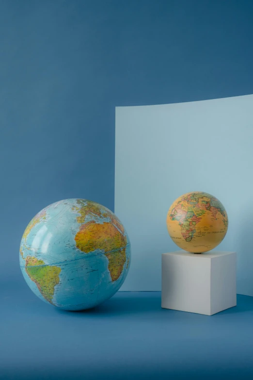 three globes on pedestals in front of a blue background, an album cover, by Alison Geissler, trending on unsplash, world map, marble material, 1960s color photograph, replica model