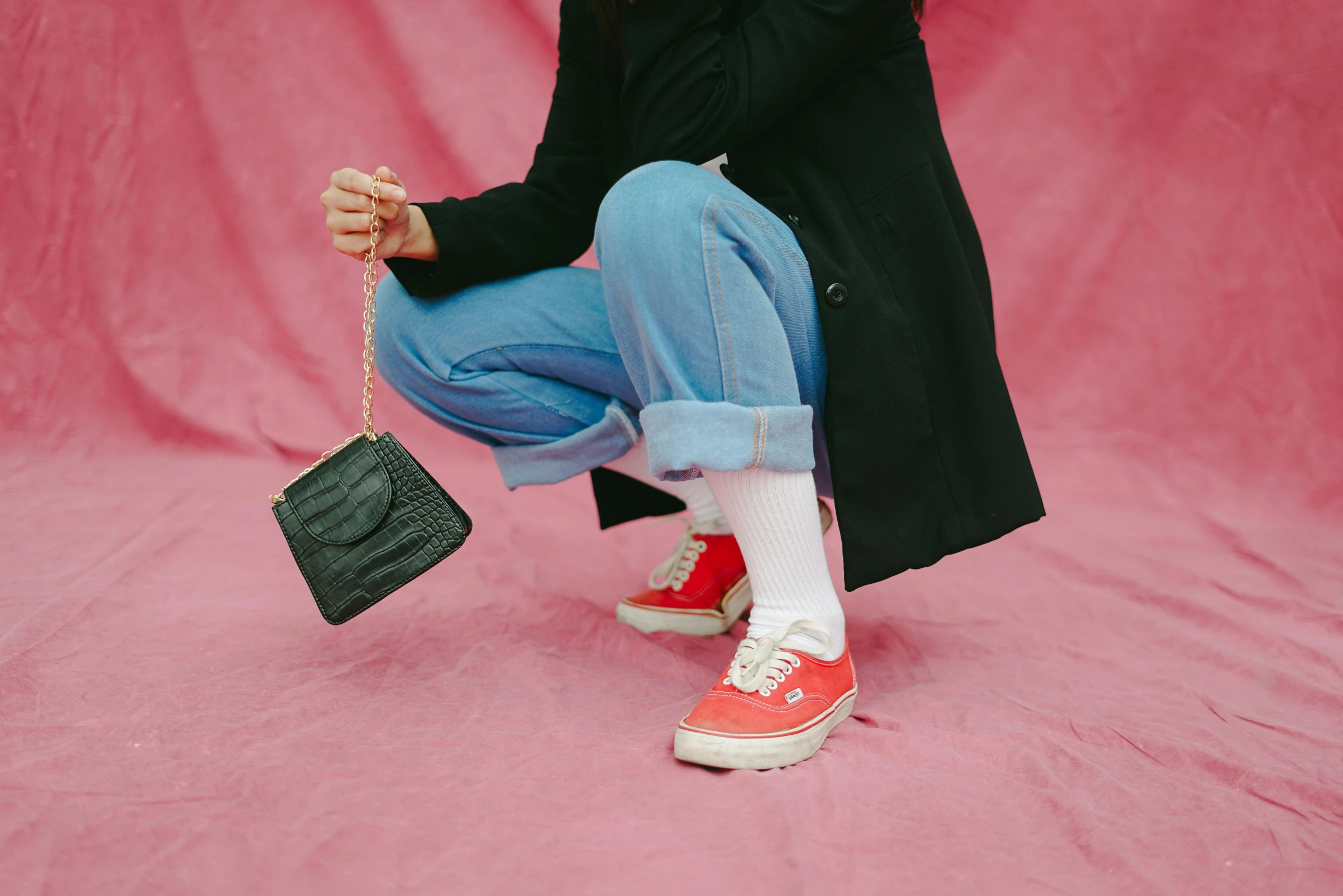 a woman kneeling on a pink surface holding a purse, trending on pexels, wearing red converse shoes, wearing jeans and a black hoodie, sneaker made out of lego, wearing a black and red suit