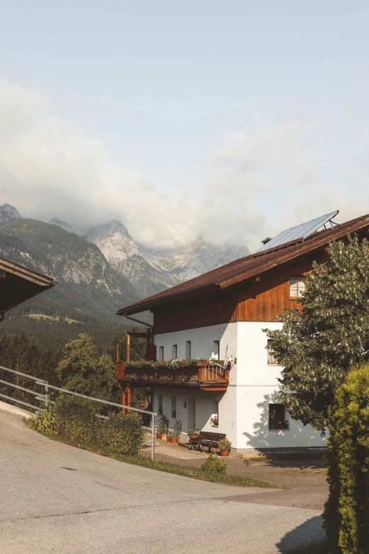 a couple of houses sitting on the side of a road, inspired by Georg Friedrich Schmidt, unsplash, mountains in background, balcony, farmhouse, sun overhead