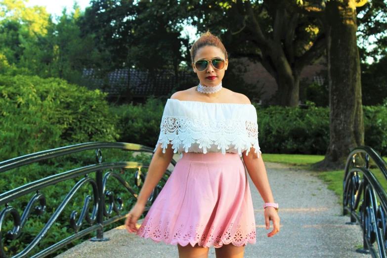 a woman standing on a bridge wearing a pink skirt, an album cover, inspired by Olivia Peguero, pexels, renaissance, white lace clothing, off the shoulder shirt, in a park, wearing a crop top