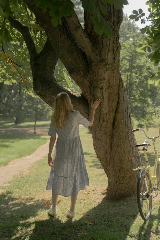 a woman standing next to a tree next to a bike, inspired by Enrique Simonet, unsplash, magic realism, still from a wes anderson movie, ignant, midsommar - t, movie footage