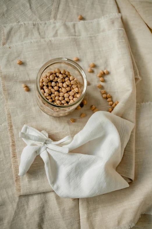 a bowl of chickpeas and a napkin on a table, a still life, by Nina Hamnett, unsplash, renaissance, beige, transparent, cotton fabric, 1 6 x 1 6