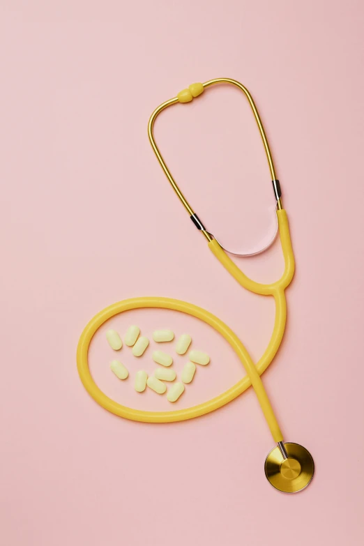 a stethoscope and pills on a pink background, by Nicolette Macnamara, yellow aureole, hero shot, goop, close full body shot