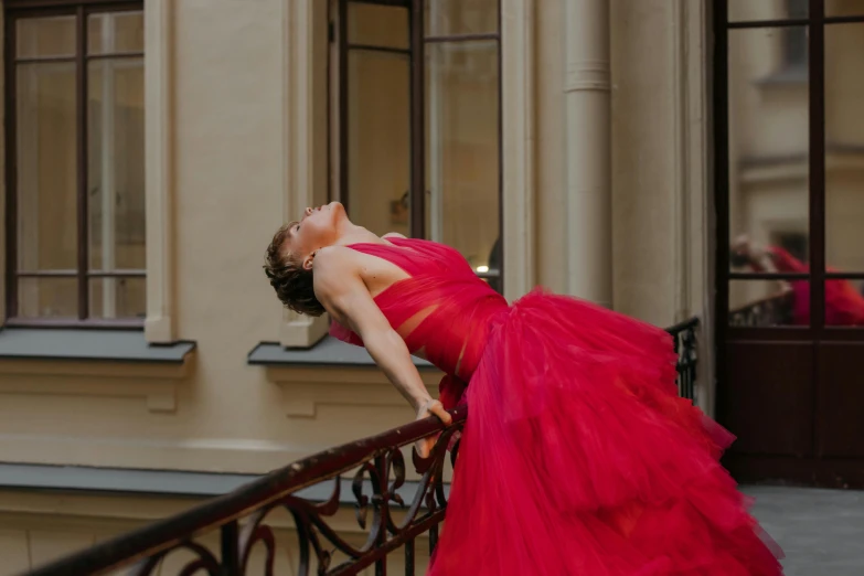 a woman in a red dress leaning on a railing, by Emma Andijewska, pexels contest winner, arabesque, wearing a pink ballroom gown, excitement, showing her shoulder from back, 15081959 21121991 01012000 4k