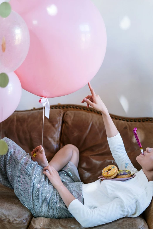 a woman laying on a couch holding a bunch of balloons, happening, pink frosted donut, at a birthday party, maternity feeling, long trunk holding a wand