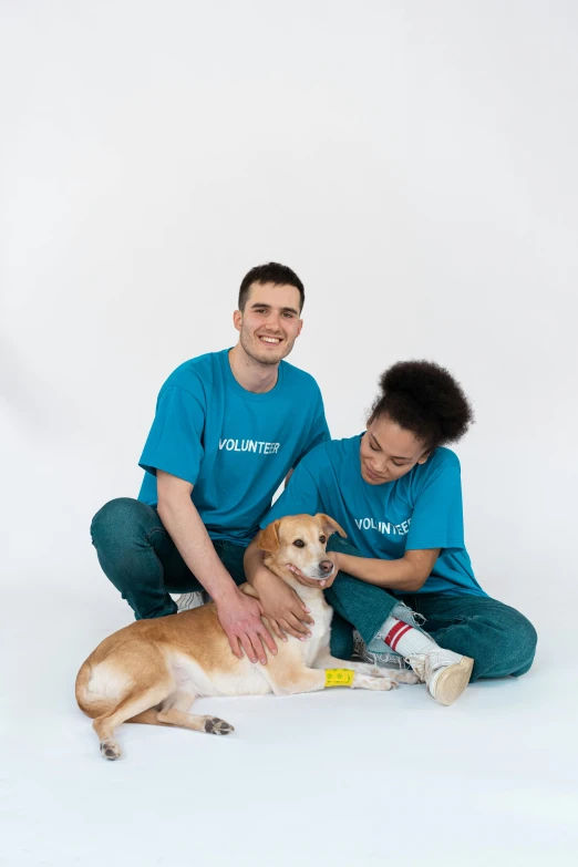 a couple of people that are sitting down with a dog, holding a staff, cyan photographic backdrop, injured, holding paws