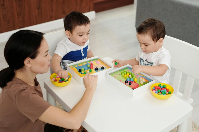 a woman sitting at a table with two children, by Eden Box, pexels contest winner, board games on a table, multi - coloured, toddler, tightly framed