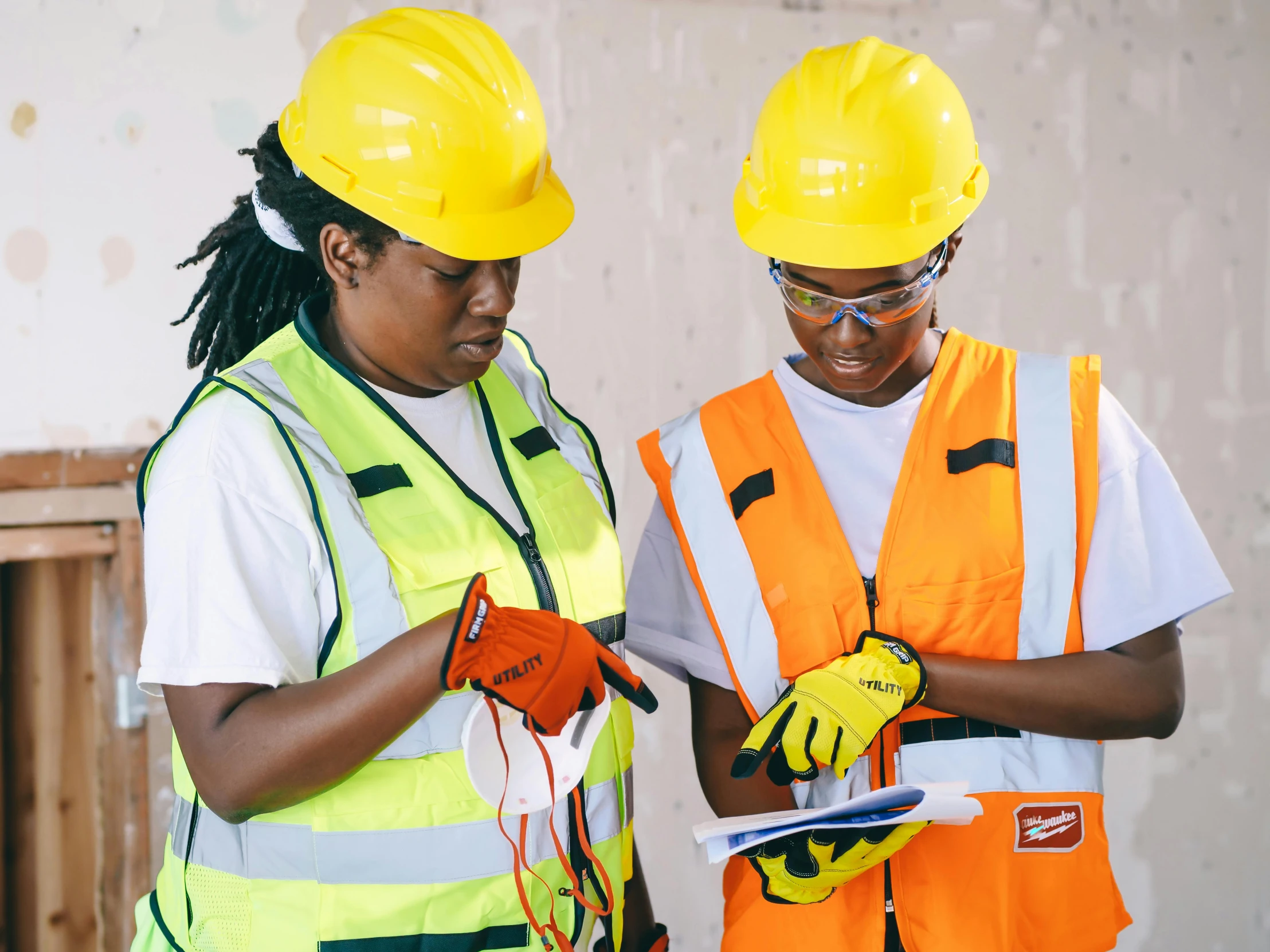 a couple of women standing next to each other, by Jeka Kemp, pexels, arbeitsrat für kunst, yellow hardhat, wearing gloves, holding a clipboard, mongezi ncaphayi