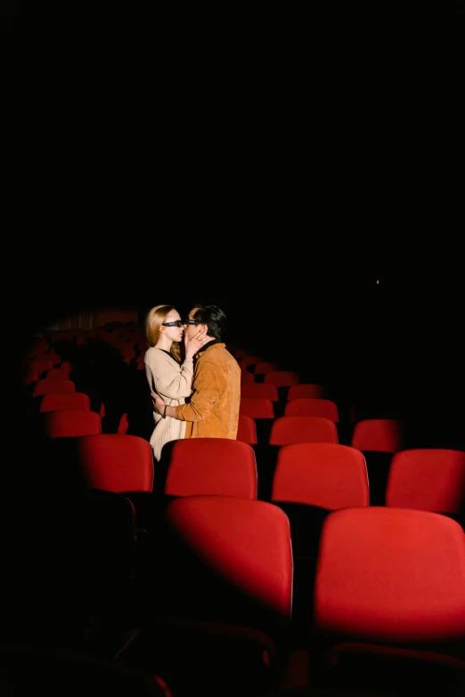 a couple standing next to each other in a theater, inspired by Nan Goldin, kiss, wes anderson movie, [ theatrical ]