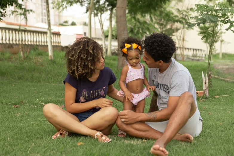 a couple of people that are sitting in the grass, by Nándor Katona, pexels, realism, 3 5 year brazilian mother, portrait of family of three, curly afro, tan skin a tee shirt and shorts