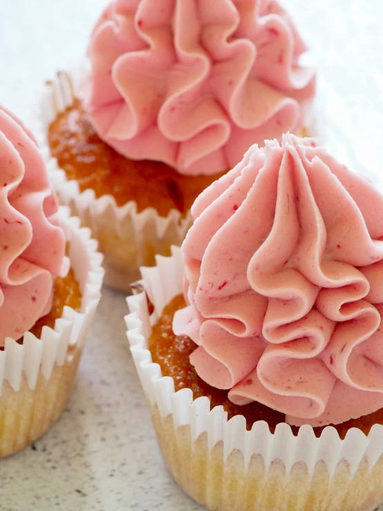 three cupcakes with pink frosting sitting on a table, inspired by Jacopo Bellini, intricate pasta waves, raspberry, thumbnail, epicurious