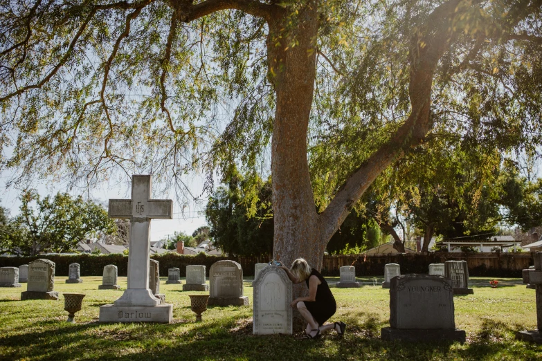 a woman sitting under a tree in a cemetery, unsplash, southern california, a person standing in front of a, ignant, lachlan bailey