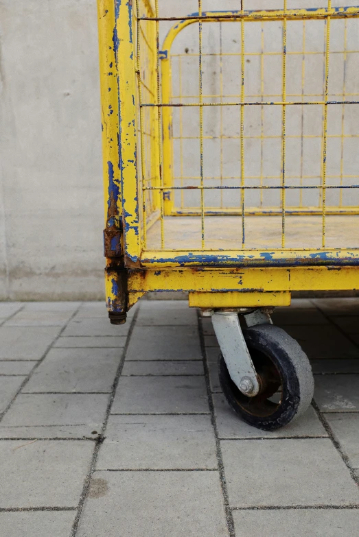 a yellow cart sitting on top of a sidewalk, by Andries Stock, unsplash, industrial design, cage, worn paint, square