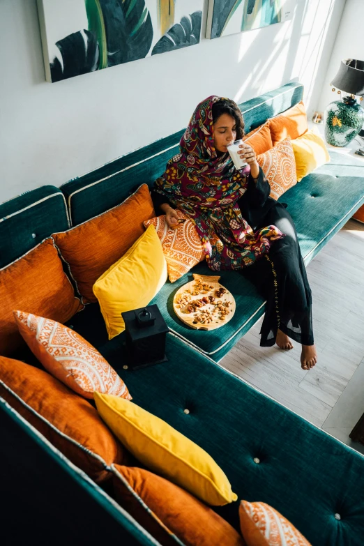 a woman sitting on a couch in a living room, inspired by Riad Beyrouti, trending on unsplash, arabesque, eating chips and watching tv, cinematic outfit photo, high angle shot, multicoloured