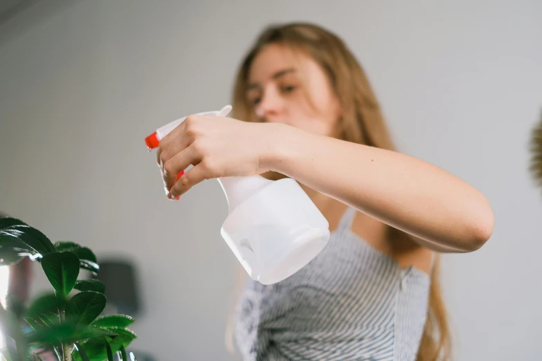 a woman holding a spray bottle next to a potted plant, pexels contest winner, profile image, white steam on the side, domestic, made of liquid