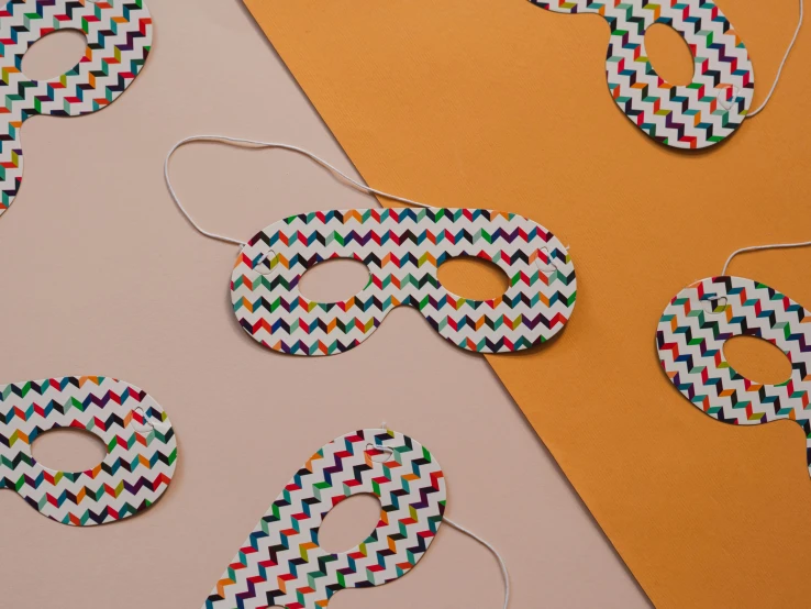 a group of paper masks sitting on top of a table, a mosaic, inspired by Bridget Riley, trending on pexels, detailed product image, multicoloured, zig zag, wearing an eye patch