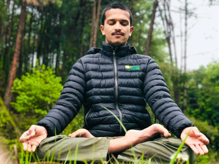a man sitting in the grass doing yoga, inspired by Kailash Chandra Meher, wearing green jacket, avatar image