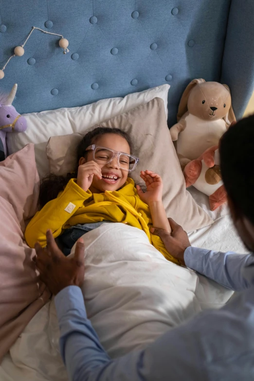 a little girl laying in a bed with stuffed animals, pexels contest winner, process art, wearing lab coat and glasses, reaching out to each other, couple on bed, healthcare