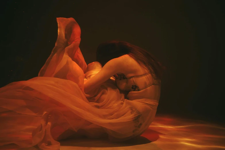 a woman in an orange dress floating in water, an album cover, inspired by Anna Füssli, figuration libre, crawling out of a dark room, draped in flowing fabric, lit from below with red lighting, sitting on the floor