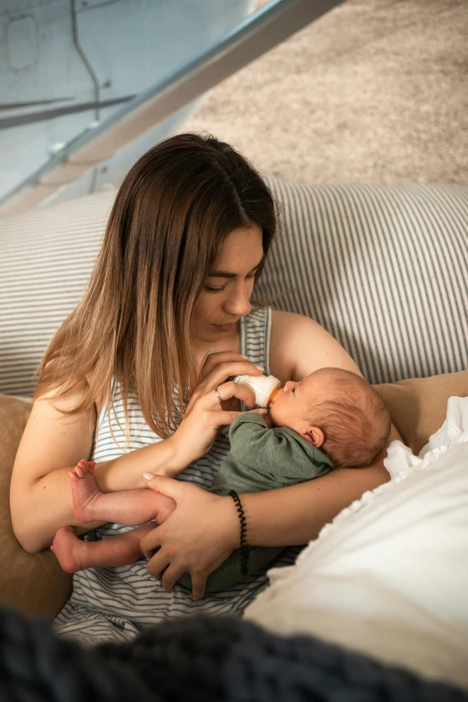 a woman sitting on a couch feeding a baby, pexels contest winner, resting on chest, liam, isabella, detailed and soft