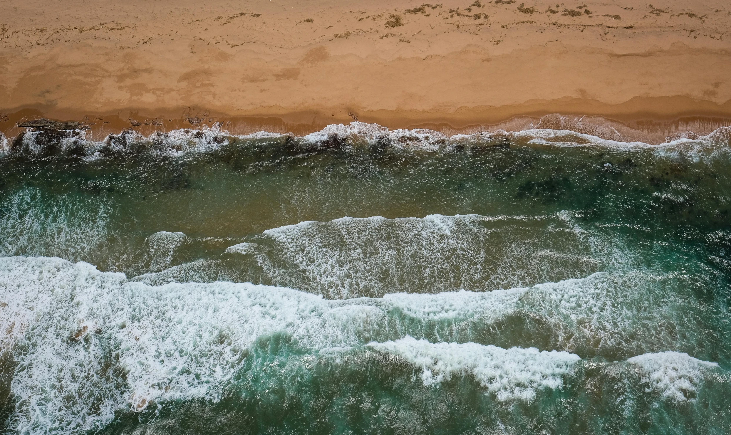 a large body of water next to a sandy beach, by Peter Churcher, pexels contest winner, close-up from above, rough seas, manly, ochre