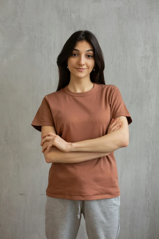 a woman standing in front of a gray wall, brown shirt, background image, in tshirt, terracotta