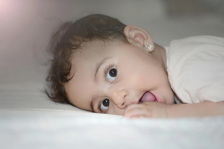 a close up of a baby laying on a bed, pexels contest winner, happening, gaping mouth, seducing expression, lights off, grey