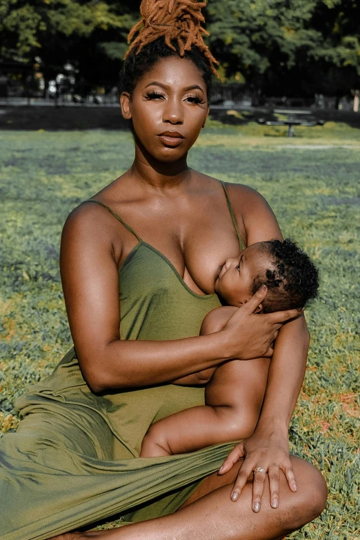 a woman in a green dress holding a baby, unsplash, covered breasts, brown skin, sitting down, instagram picture