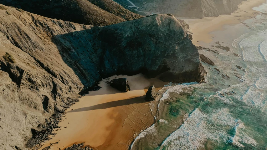 a man standing on top of a sandy beach next to the ocean, by Lucas Vorsterman, pexels contest winner, “ aerial view of a mountain, massive arch, caramel. rugged, thumbnail
