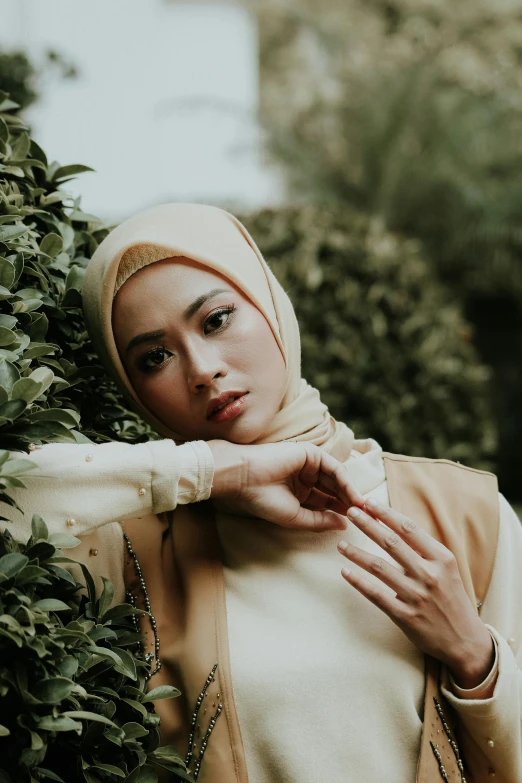 a woman wearing a hijab poses for a picture, by Basuki Abdullah, trending on pexels, hurufiyya, beige and gold tones, greenery, seductive expression, at a fashion shoot