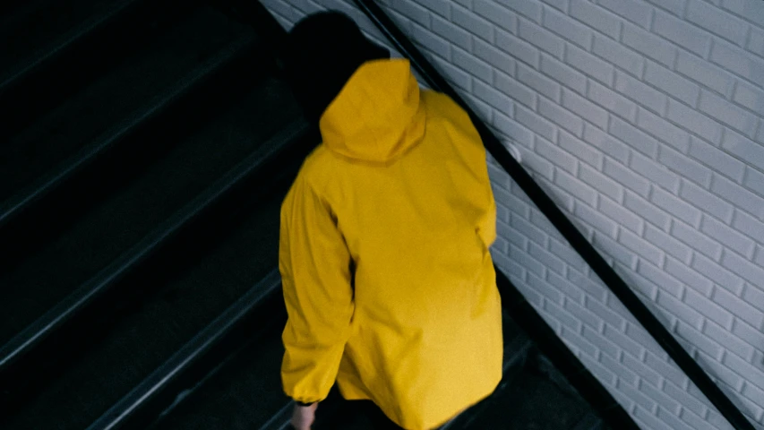 a person in a yellow jacket walking up a flight of stairs, unsplash, wearing hood, looking down, clothing drop, rectangle