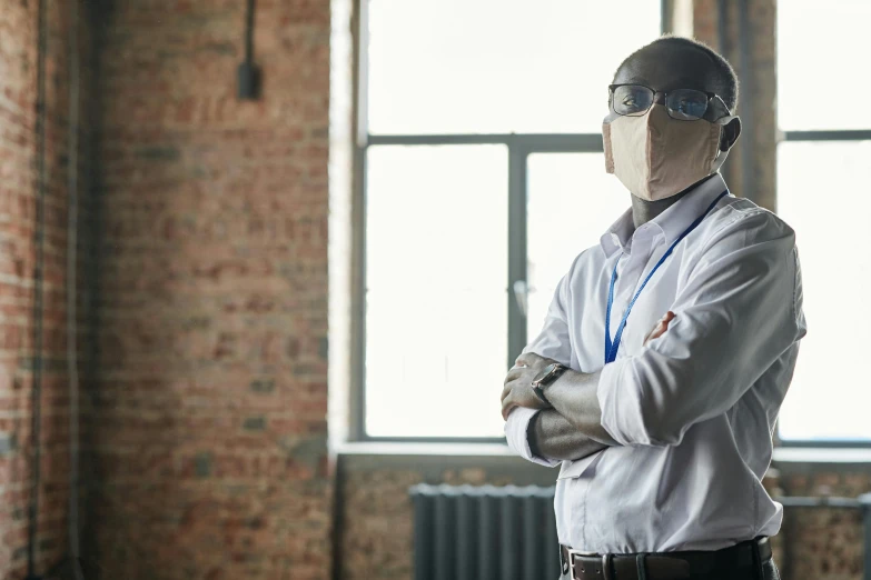 a man wearing a mask standing in front of a window, in a workshop, hero, white lab coat, architect