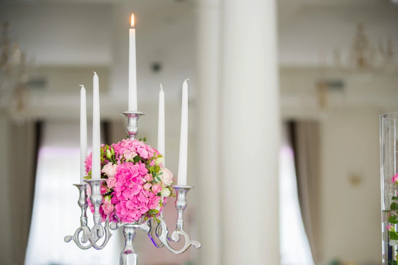 a vase filled with pink flowers sitting on top of a table, holding a candle holder, multiple stories, event, chandelier