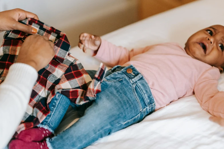 a woman holding a baby laying on top of a bed, by Nina Hamnett, trending on pexels, incoherents, wearing jeans, boy and girl, pink clothes, holding hands